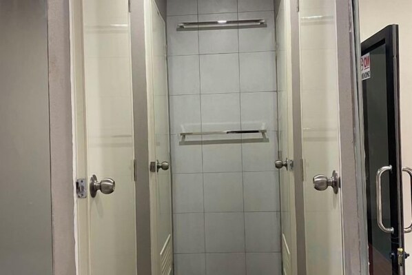 A corridor with glass doors leading to a bathroom with a tiled floor and a towel rack. - Hide Hostel (Koh Phangan)