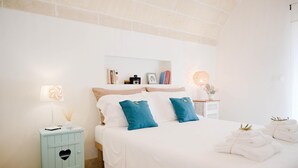 A bedroom with a bed, a nightstand, a lamp, and a shelf with books and a camera.