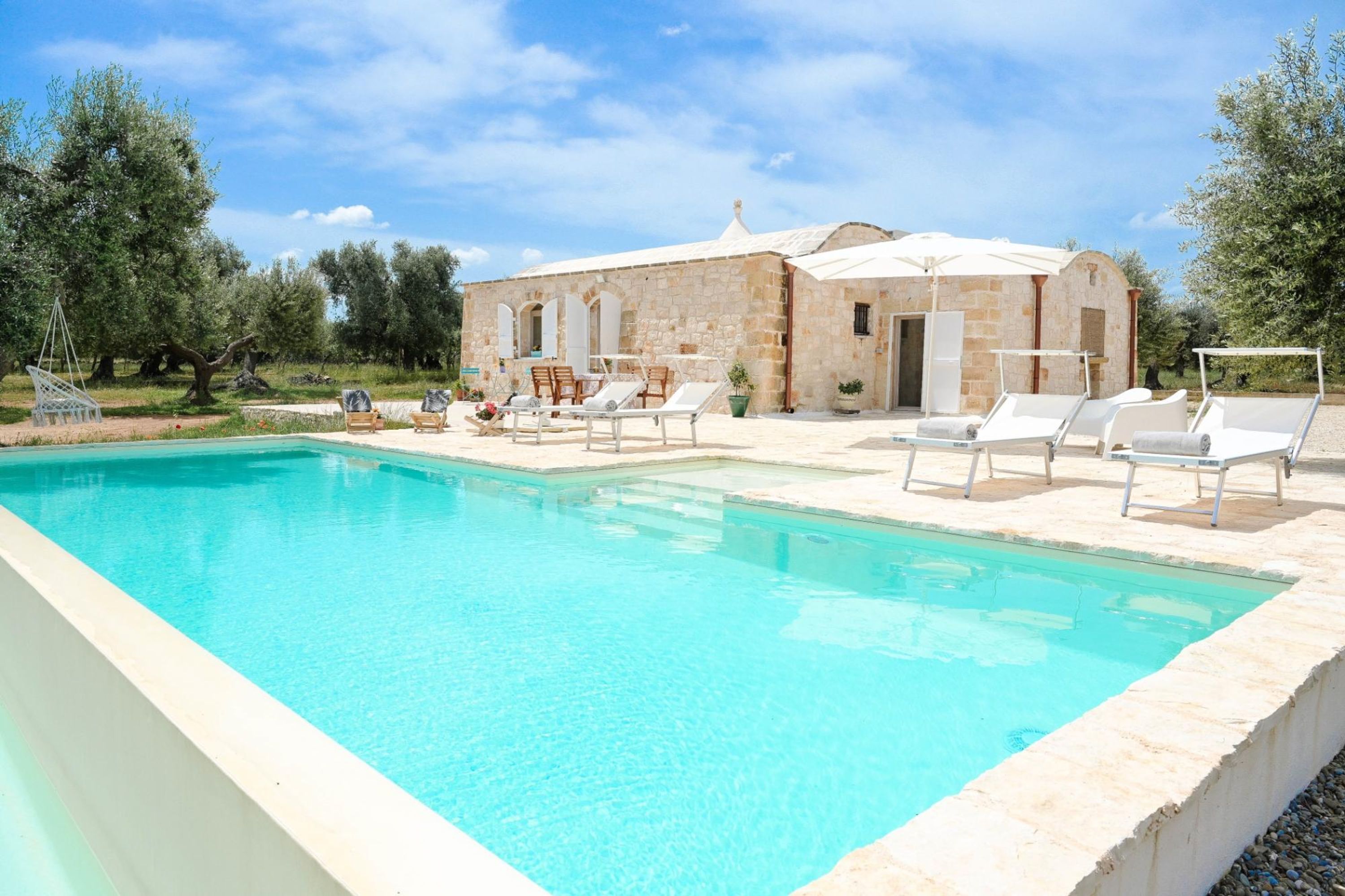 A swimming pool with lounge chairs and a stone building with arches.