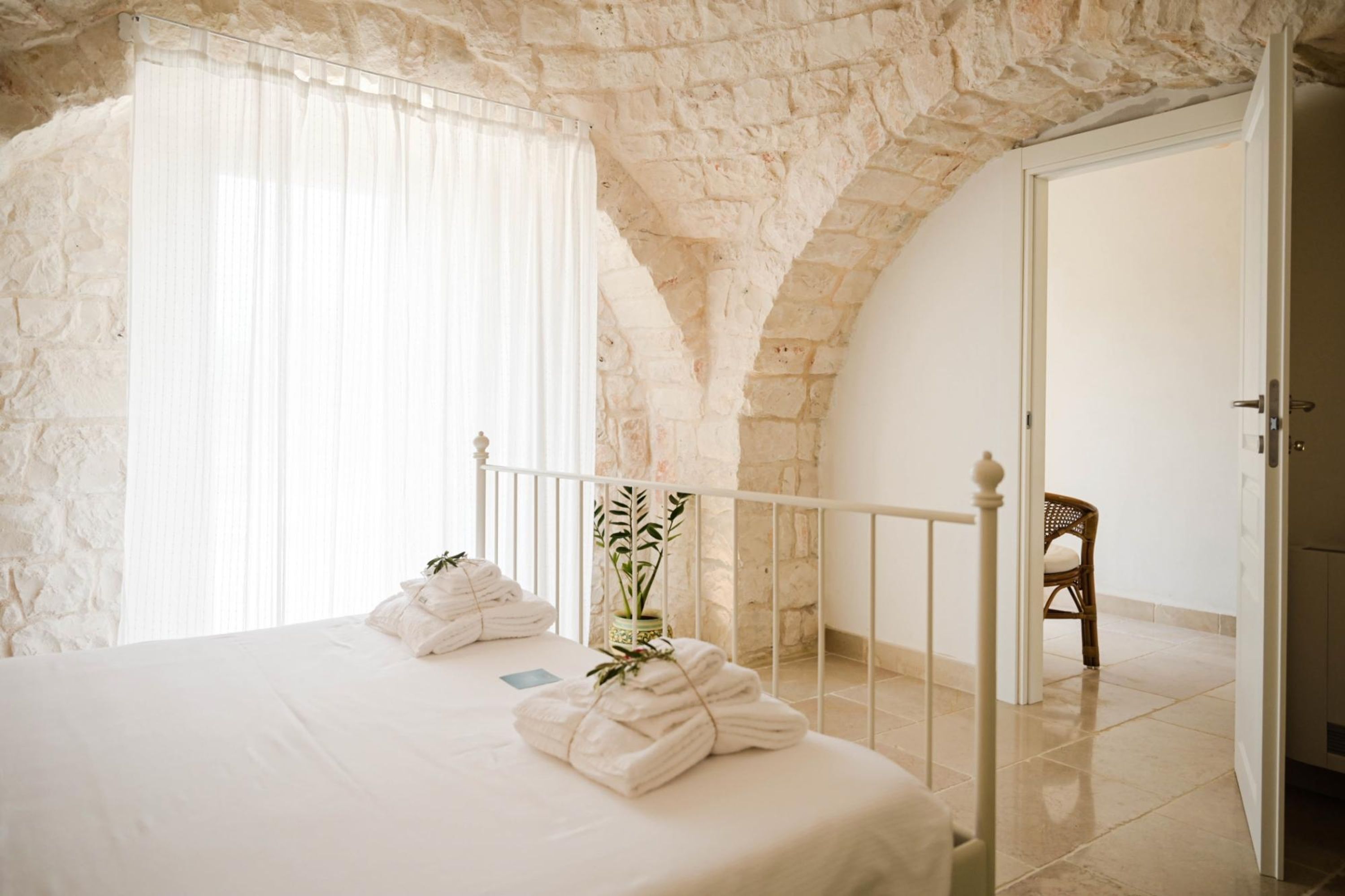 Un dormitorio con techo de piedra, una cama con ropa blanca, una planta en maceta y una silla.