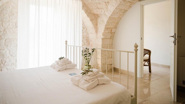 A bedroom with a stone ceiling, a bed with white linens, a potted plant, and a chair.