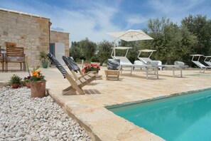 A poolside area with lounge chairs, a table, and a stone building. - Trullo Delori (Villa Castelli)