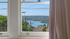 A view through a window with a clear sky, power lines, and a distant body of water. - Harbour Grove Sanctuary w Garage , Quiet & Private (Cremorne)