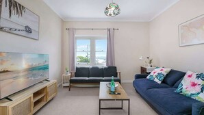 A modern living room with a flat-screen TV, a sofa, a coffee table, and a large window with curtains. - Harbour Grove Sanctuary w Garage , Quiet & Private (Cremorne)