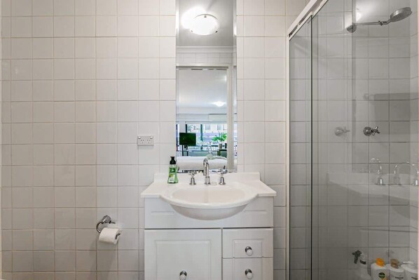 A modern bathroom with a white sink, mirror, and glass shower enclosure.