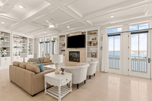 Un salon spacieux avec un canapé beige, des fauteuils blancs, une cheminée et un grand téléviseur.