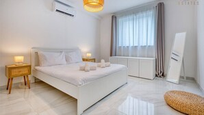 Une chambre moderne avec un grand lit, des lampes de chevet, un luminaire suspendu, une fenêtre avec des rideaux et un miroir.