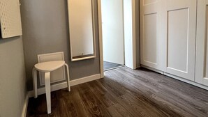 A hallway with a wooden floor, a white chair, a large mirror, and a white door.