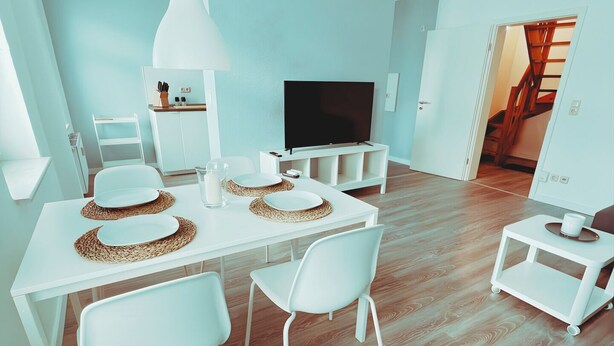 A modern living room with a dining area, a flat-screen TV, and a staircase leading to another level.