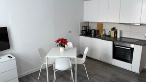 A modern kitchen with white cabinets, a dining table with chairs, a coffee maker, and a TV on a stand. - Close to downtown | Parking | Up to 4 guests (Chemnitz)