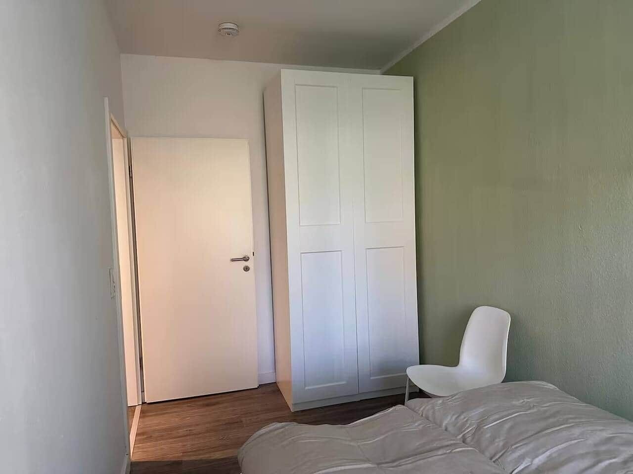 Une chambre à coucher avec un lit, une chaise blanche, une armoire et une porte.