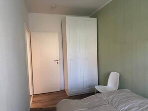 A bedroom with a bed, a white chair, a wardrobe, and a door.