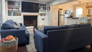 A living room with a fireplace, a television, and a kitchen area with a refrigerator and microwave. - Luxury Townhouse near Downtown and Beaches with Hot Tub (Mount Pleasant)