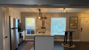 A kitchen with a refrigerator, oven, microwave, and a window with blinds. There is a sink, a countertop, and a small table with a chair. - Luxury Townhouse near Downtown and Beaches with Hot Tub (Mount Pleasant)
