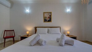 Een hotelkamer met een groot bed, twee bedlampen, een houten stoel en een schilderij aan de muur.