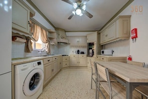 A compact kitchen with a washing machine, microwave, and a ceiling fan. - Authentic Maltese 3BR home with Terrace in Mosta! (Mosta)