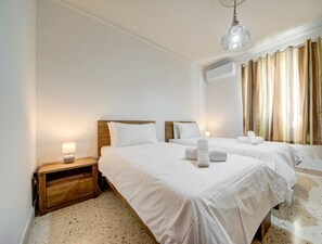 A hotel room with two beds, a wooden nightstand, a lamp, and a large window with curtains. - Authentic Maltese 3BR home with Terrace in Mosta! (Mosta)