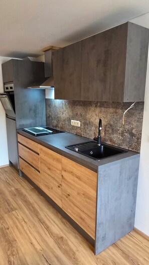 A modern kitchen with a central island, wooden cabinets, and a grey countertop. - Ferienhaus Schwendehof (Fontanella)