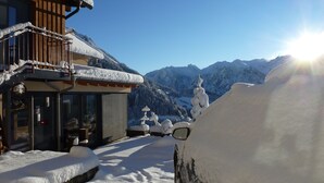 Une station de montagne enneigée, avec un bâtiment en bois, une entrée en verre et une vue sur des sommets couverts de neige.