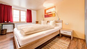 Une chambre à coucher avec un lit en bois, une table de chevet, une fenêtre avec des rideaux rouges et un tableau accroché au mur.