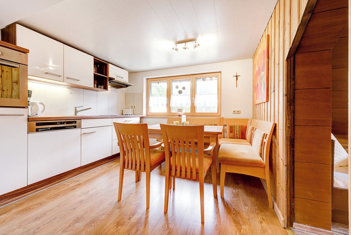 Eine moderne Küche mit weißen Schränken, Holzböden und einem Essbereich mit Holzstühlen und einer Bank.