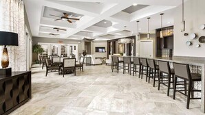 A spacious dining area with a long table and chairs, a ceiling fan, and a modern kitchen with a bar. - 7049 Solterra 6 bedrs 18guests pool summer kitchen (Davenport)