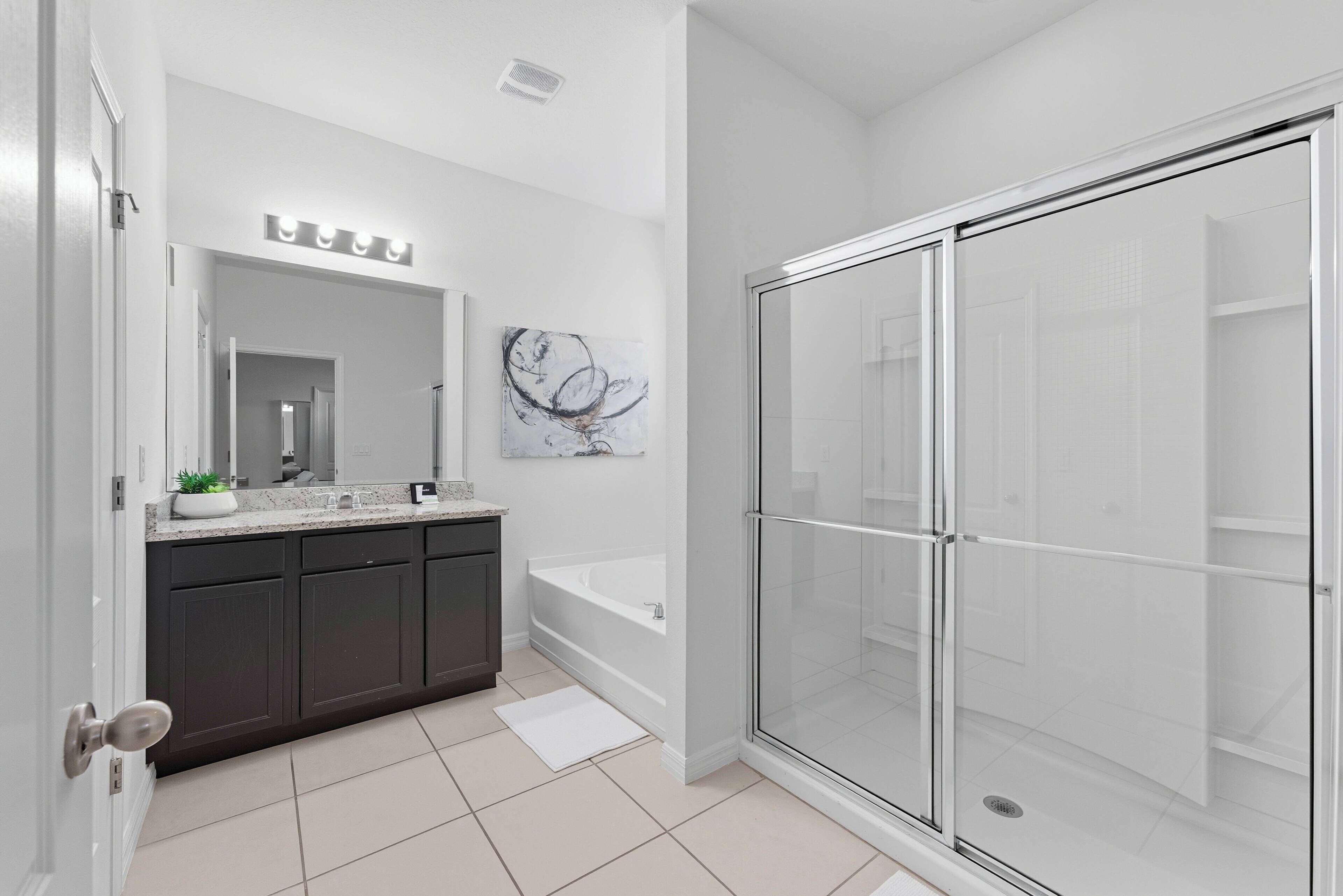 A modern bathroom with a dark-toned vanity, a large mirror, a bathtub, and a glass-enclosed shower.