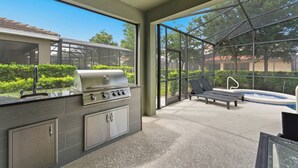 An outdoor kitchen with a grill, a built-in sink, and a view of a swimming pool and lounge chairs. - 7049 Solterra 6 bedrs 18guests pool summer kitchen (Davenport)