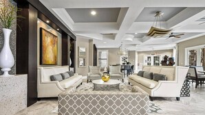 A spacious living room with a large painting, two sofas, a coffee table, and a patterned ottoman. - 7049 Solterra 6 bedrs 18guests pool summer kitchen (Davenport)