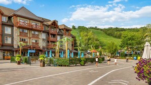 A hotel with a stone facade, multiple balconies, and a paved courtyard with umbrellas. - Family Townhome at Blue with Resort Shuttle (The Blue Mountains)