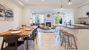 A spacious kitchen with a central island, a dining area with a long wooden table, and a cozy seating area with a fireplace. - Family Townhome at Blue with Resort Shuttle (The Blue Mountains)