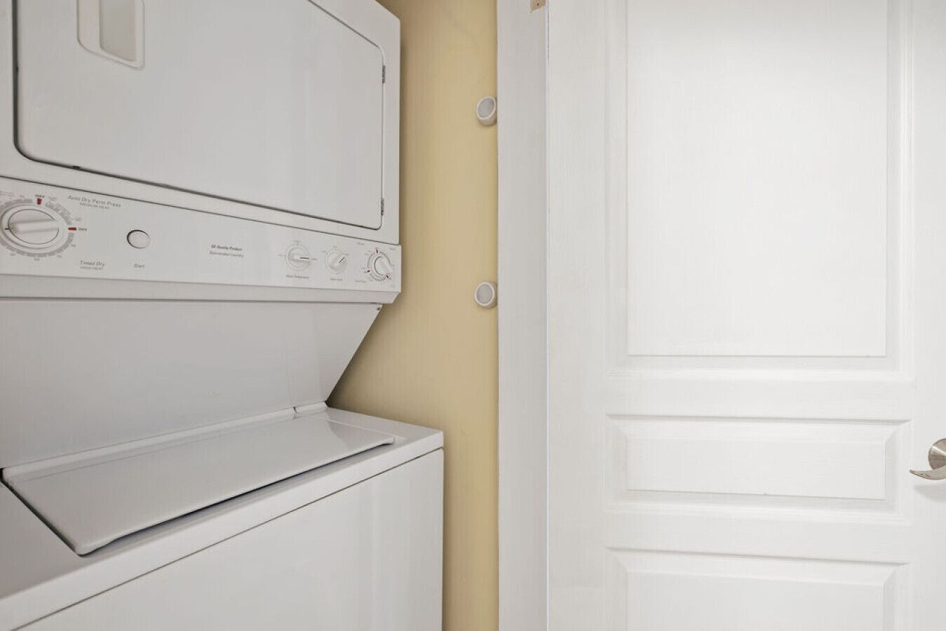 A white stacked washer and dryer unit with control knobs and a door.