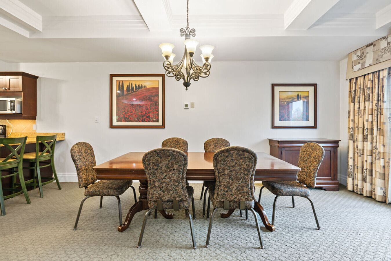 Une salle à manger avec une table en bois et des chaises à motifs, un lustre et des œuvres d’art encadrées accrochées aux murs.