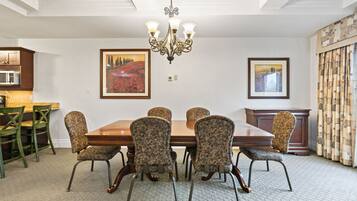 Une salle à manger avec une table en bois et des chaises à motifs, un lustre et des œuvres d’art encadrées accrochées aux murs.