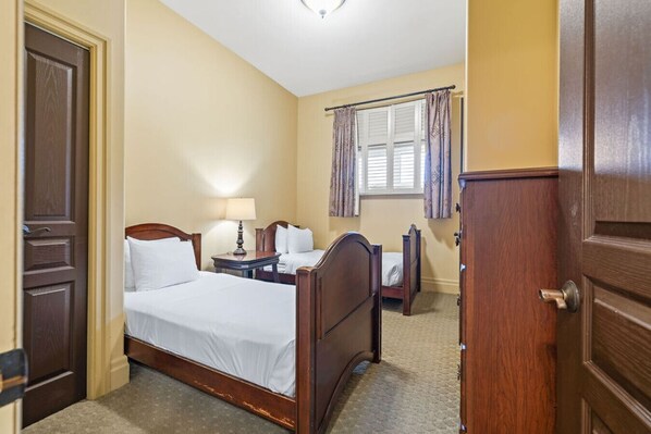 A hotel room with a double bed, a bedside table with a lamp, a small desk with a chair, a wardrobe, and a window with curtains.