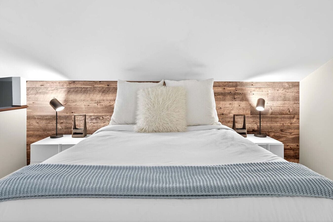 Une chambre à coucher moderne avec une tête de lit en bois, une literie blanche, deux lampes de chevet et un oreiller moelleux.