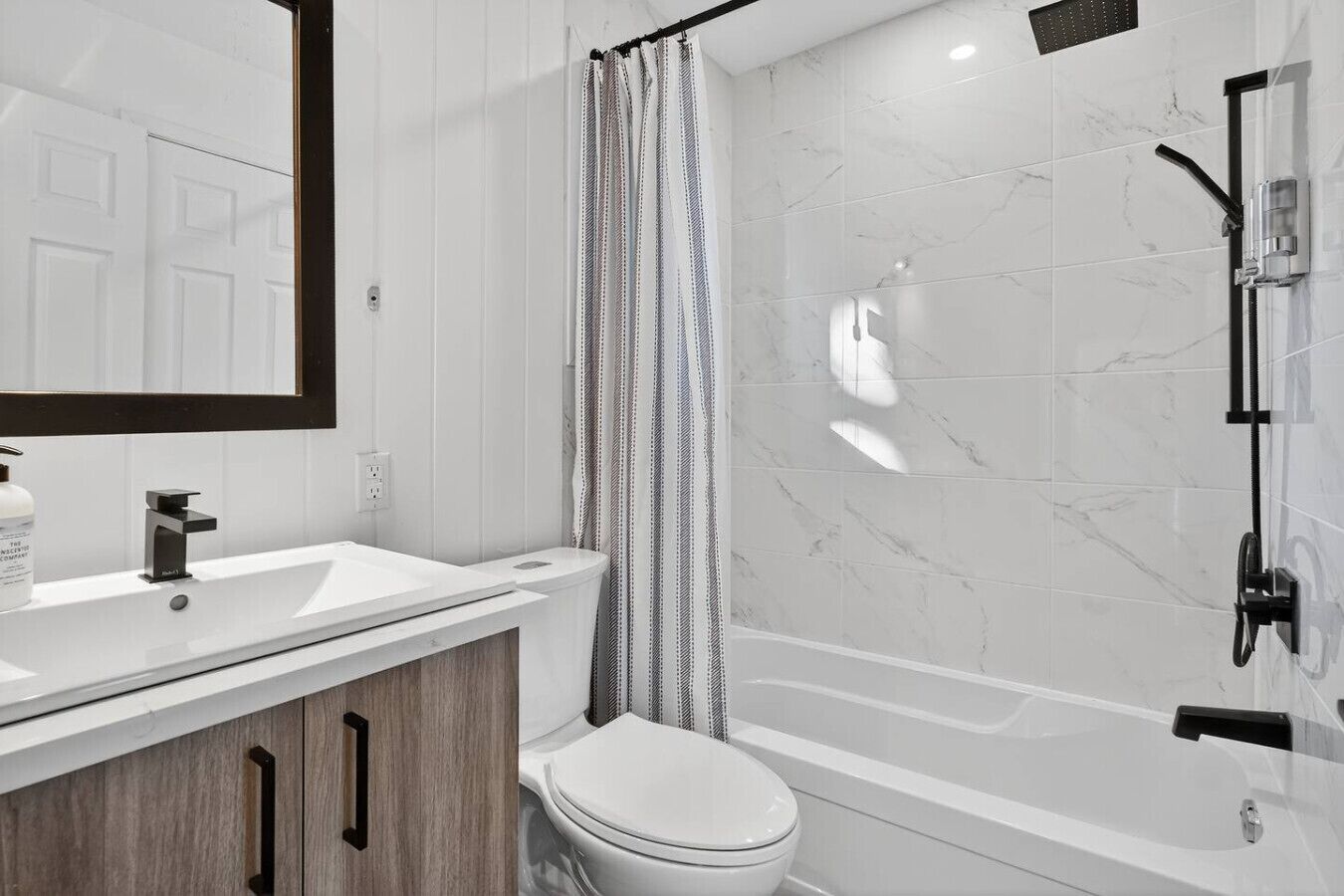 Ein modernes Badezimmer mit einem weißen Waschtisch, einer Toilette, einer Dusche mit Glastür und einer Wand mit Marmorplatten.