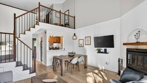 A spacious living area with a wooden staircase, a dining table with chairs, a sofa, and a fireplace.