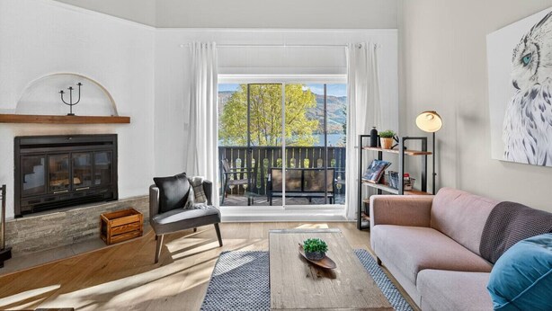 A modern living room with a fireplace, a sofa, a coffee table, and a view of a balcony with outdoor furniture.