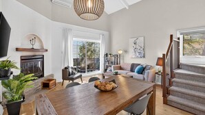 A spacious living area with a wooden dining table, a fireplace, a sofa, and a staircase leading to an outdoor deck.