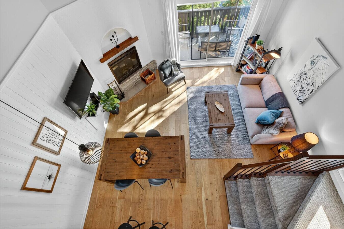 Een ruime woonkamer met houten vloer, een bank, een salontafel en een televisie. Er is een trap die naar een verdieping leidt.