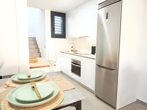 Une cuisine compacte dotée d’un réfrigérateur en acier inoxydable, d’un petit plan de travail et d’un coin repas avec une table dressée pour deux personnes.