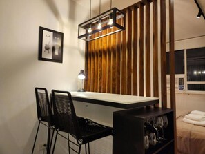 Une cuisine moderne avec un mur d’accent en bois, un coin bar avec deux chaises noires et un luminaire suspendu.