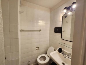 Une petite salle de bain propre, avec des carreaux blancs, des toilettes, un lavabo et un miroir.