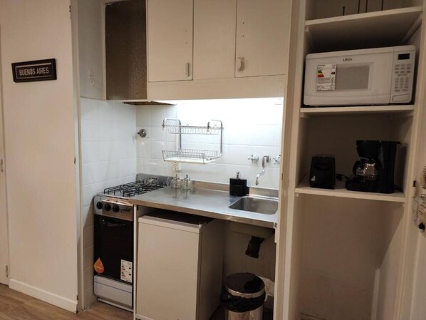 A compact kitchen with a gas stove, a microwave, a coffee maker, and a trash bin.