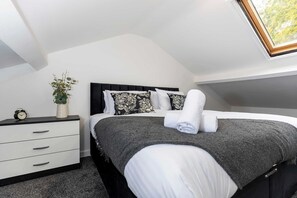 Un dormitorio con cama, mesita de noche, planta y tragaluz.