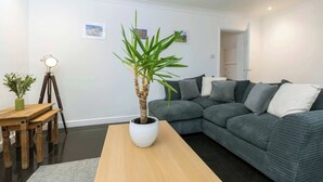 Een moderne woonkamer met een grijze bank, een houten salontafel en een plant in een pot.