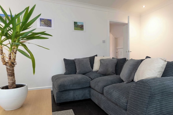 A modern living room with a grey sectional sofa, a potted plant, and two framed pictures on the wall.