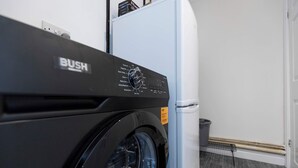 Een voorzichtsperspectief van een wasmachine met bedieningspaneel, een witte koelkast en een prullenbak in een wasserij.