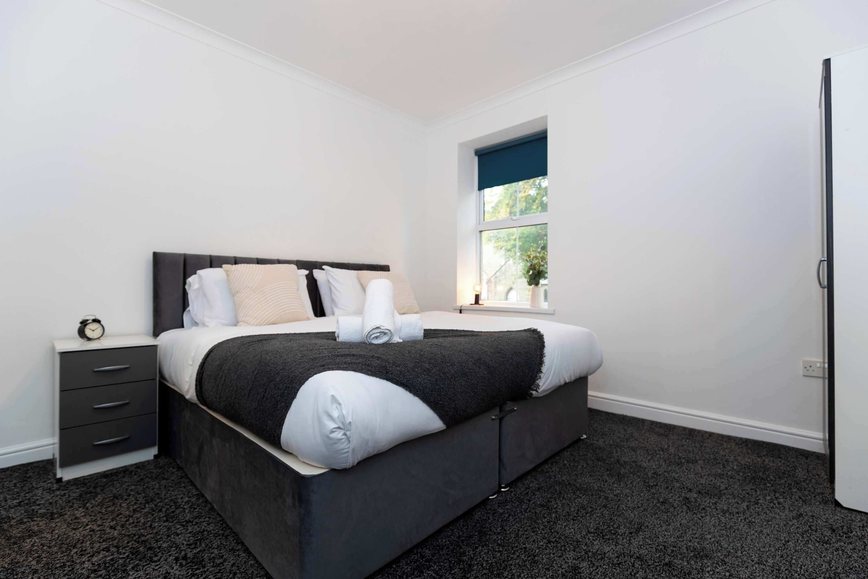 A modern bedroom with a large bed, a nightstand, a window with a view, and a door.